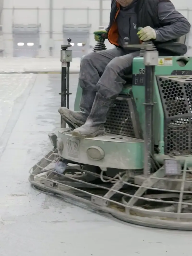 Operator running an industrial floor machine across a concrete slab